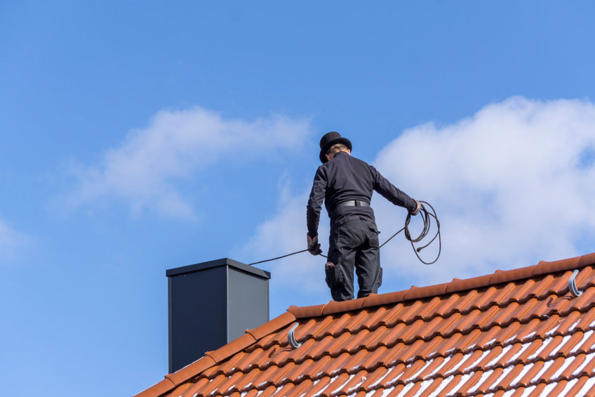 Chimney sweep cleaning a chimney standing on the house roof, lowering equipment down the flue