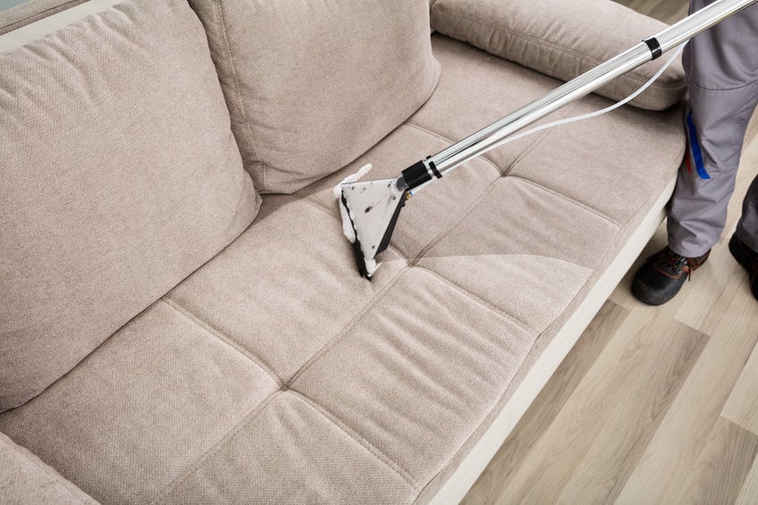 High Angle View Of A Person Cleaning Sofa With Vacuum Cleaner